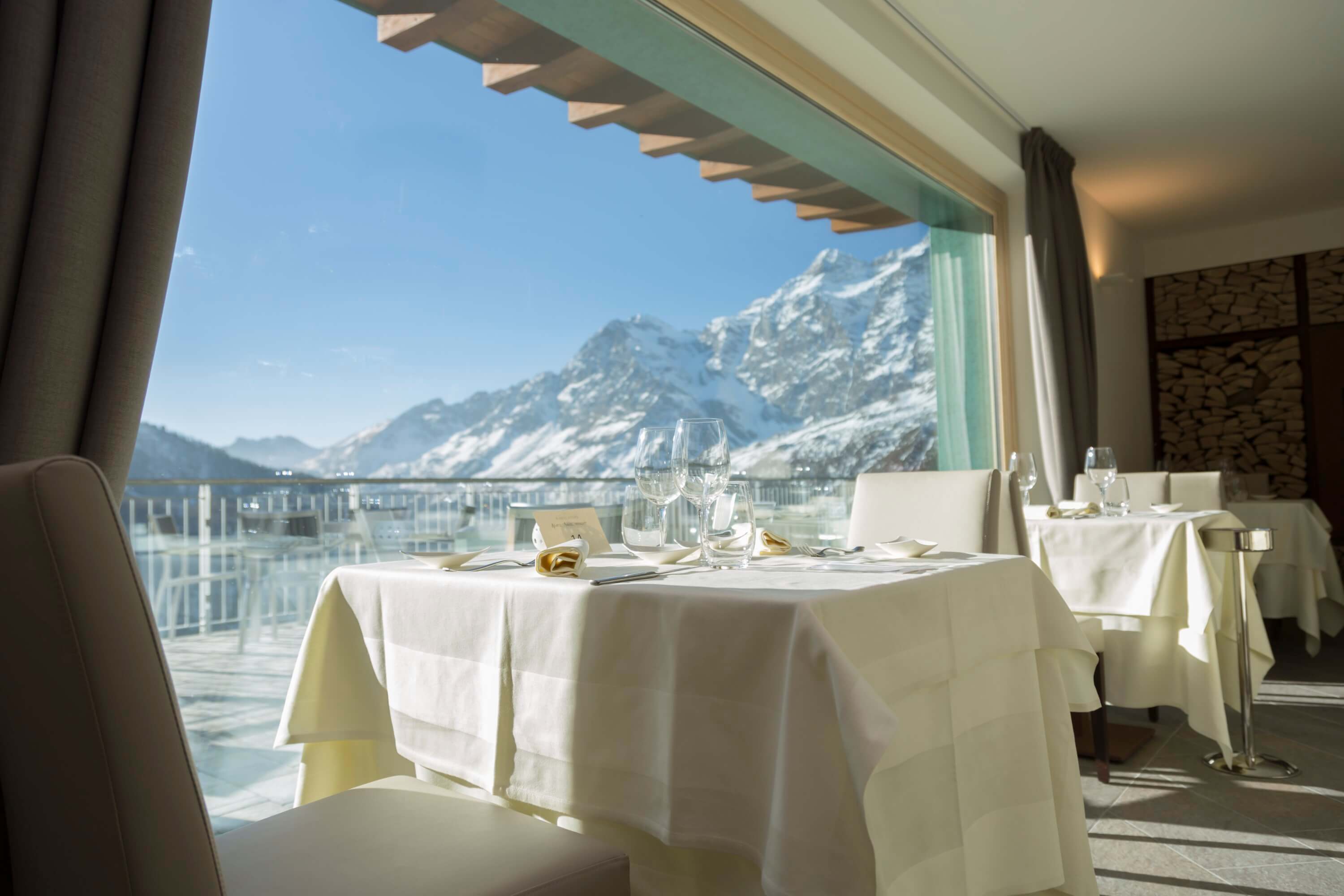 Elegant dining room with a table set for two, large window view of snow-capped mountains, and minimalist decor.